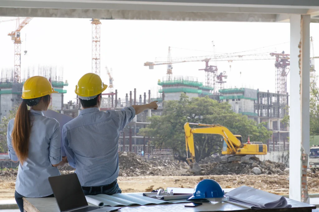 Dua insinyur mengawasi operasional ekskavator di lokasi proyek pembangunan infrastruktur.